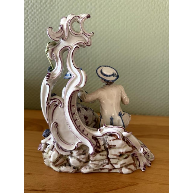 The group of figures depicts an elegant couple seated on a richly decorated, naturalistic base. The gentleman is dressed...