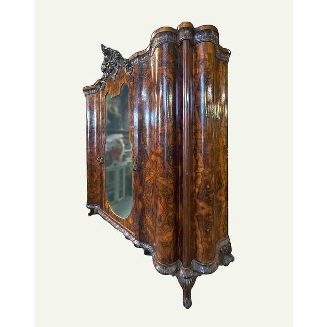 Antique Italian burl walnut bombe armoire from the late 19th century, featuring a carved crest and a central beveled glass...
