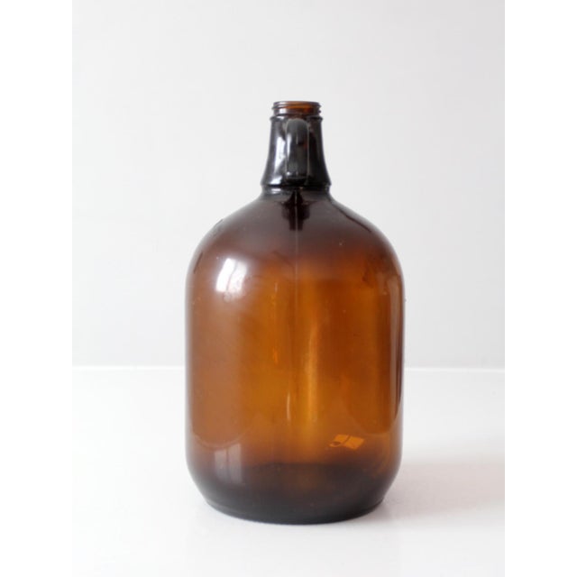 A vintage mid-century one-gallon glass jug with an integral finger-loop handle and embossed measurement markings. The...