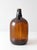 A vintage mid-century one-gallon glass jug with an integral finger-loop handle and embossed measurement markings. The...