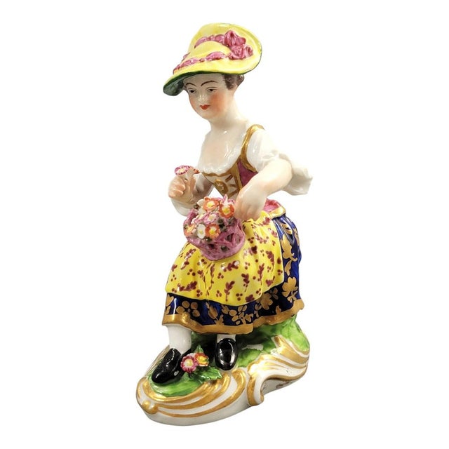 A Derby porcelain figure of a seated flower seller, dating to circa 1780–1784. The figure holds two flowers and a basket...