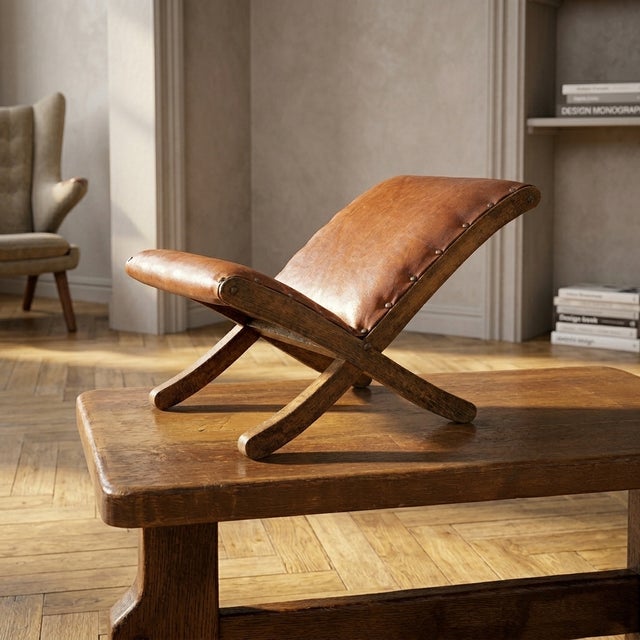 A beautifully shaped vintage footstool featuring warm brown leather upholstery and a sculptural wooden frame. Its curved...