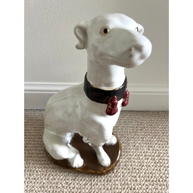 Beautifully detailed and glazed ceramic statue of a white greyhound with decorative fringed collar. He is seated on a...