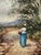Original watercolor on paper depicting a solitary woman walking along a rustic country path beneath tall trees, with...