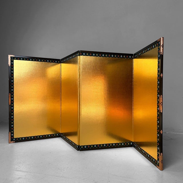 An elegant Japanese folding screen with four gold-colored panels, framed by a black-lacquered wooden frame finished with...
