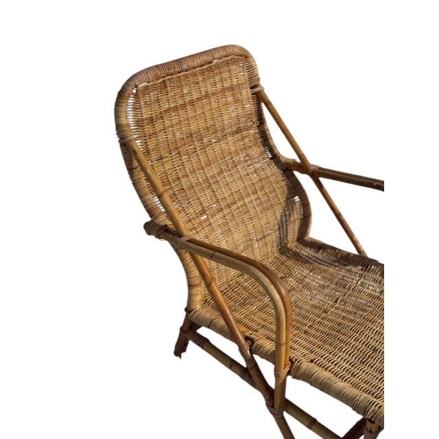 Vintage rattan chaise lounge dating to the 1970s. The piece features a sculptural bent rattan frame with integrated arms...