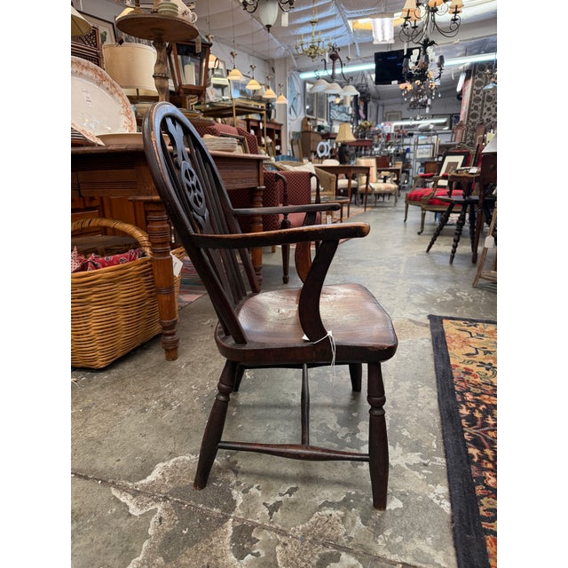 This authentic antique fireside chair features a high, hooped backrest centered by an iconic, hand-pierced "wheelback"...