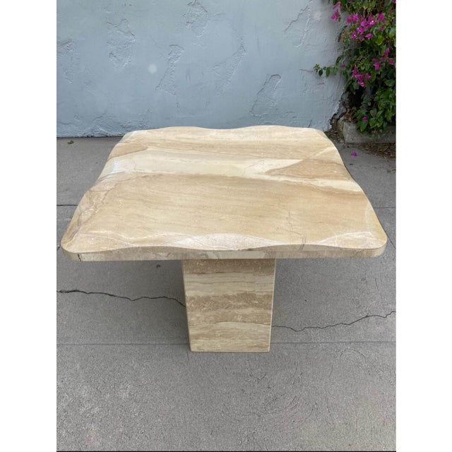 Sculptural travertine side table featuring a solid rectangular pedestal base topped with a softly contoured slab surface....