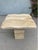 Sculptural travertine side table featuring a solid rectangular pedestal base topped with a softly contoured slab surface....