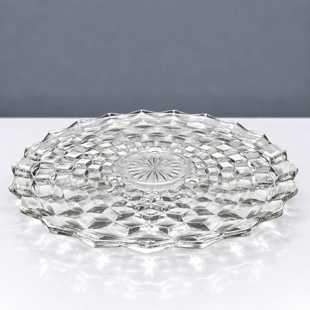 • Fostoria American #2056 three-footed cake/torte plate with geometric cube pattern and sawtooth rim. • Made in the USA;...