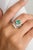 This amazing engagement ring features a creative design, highlighting a stunning emerald at its center, surrounded by...