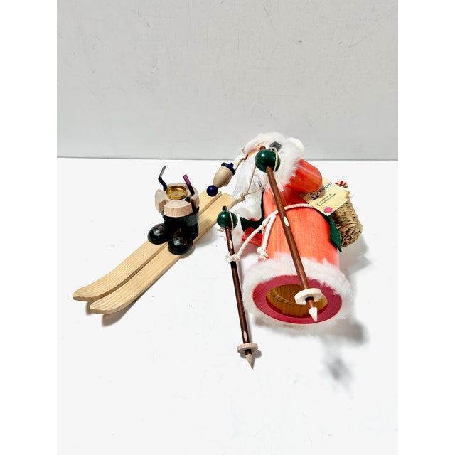 A charming Christian Ulbricht German Santa smoker figure featuring Santa Claus skiing with a basket of toys, lantern, and...