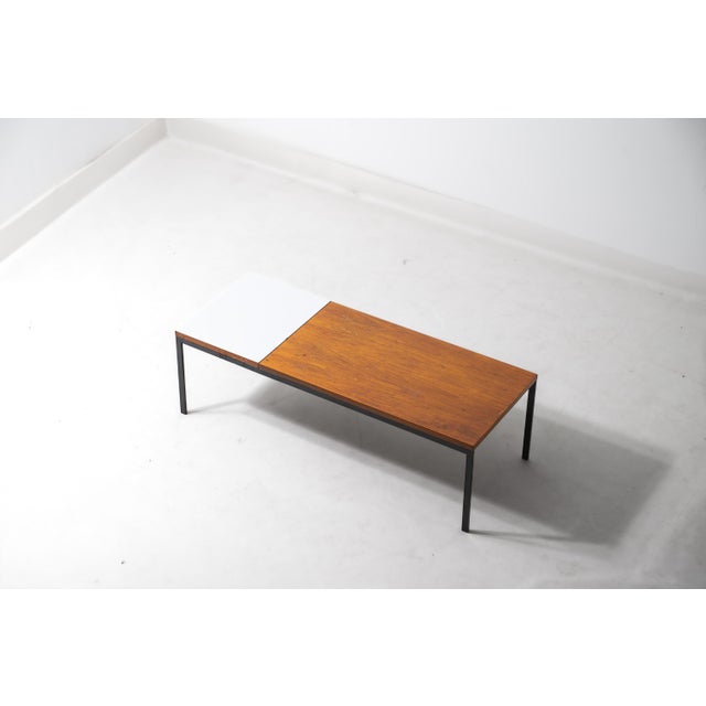 Rectangular modernist coffee table pairing a teak top with a white laminate insert, set on a slim black square-section...