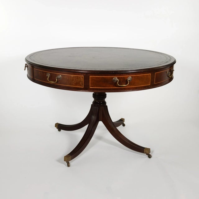 An English mahogany drum table with embossed leather top, brass hardware, and satinwood inlay on the drawer fronts. The...