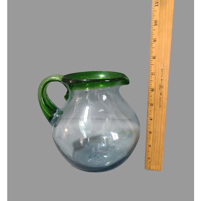 This Mexican hand-blown art glass pitcher is a true masterpiece. The attached handle and festive green rim add an element...