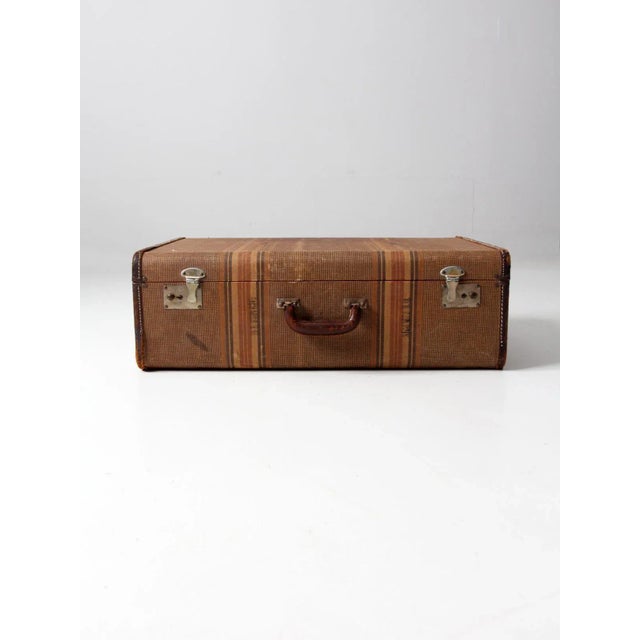 This is a vintage luggage piece. The striped canvas suitcase features brown leather trim and a leather covered handle....