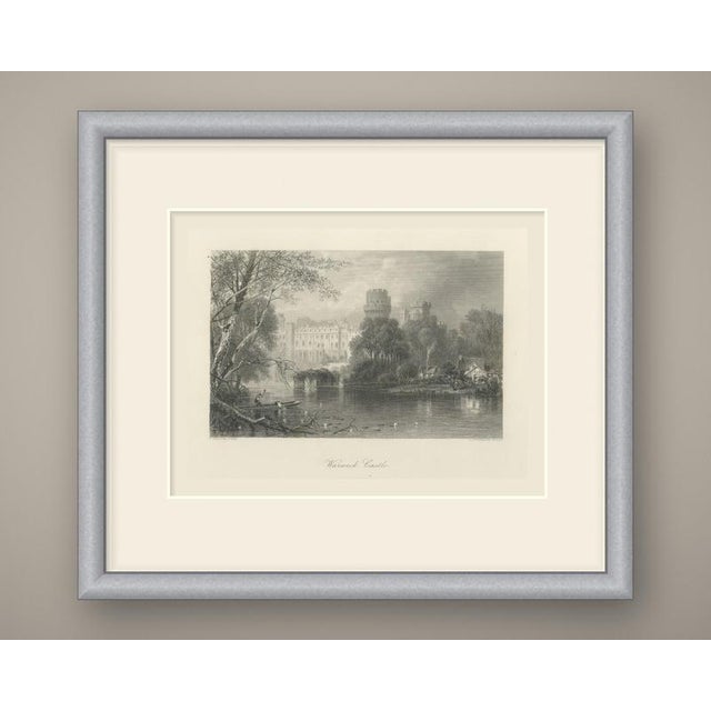 Warwick Castle is seen from the river in this steel engraving, its long battlemented range of buildings rising above the...