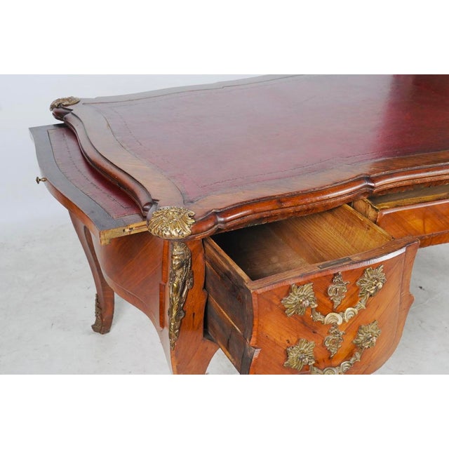 A grand French bureau plat combining warm parquetry, an oxblood tooled-leather writing surface, five drawers, and...