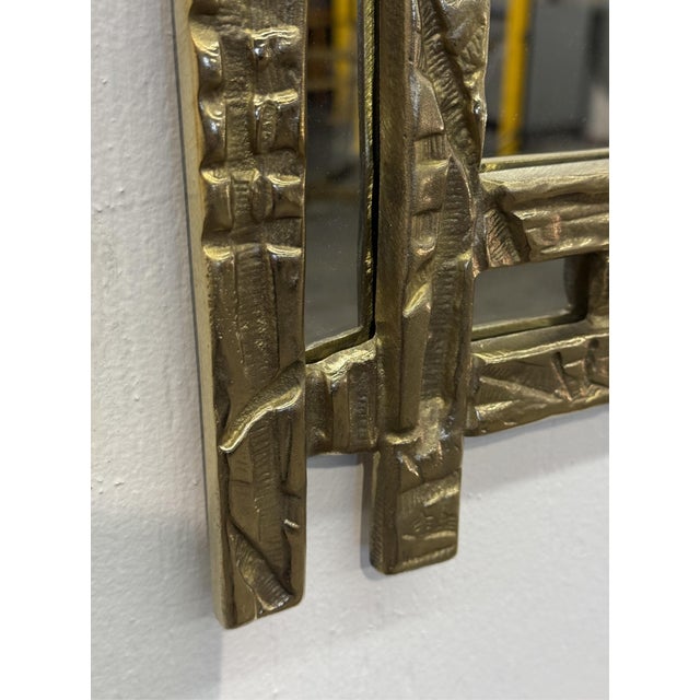 A bold and architectural wall mirror designed by Angelo Brotto, distinguished by its richly textured cast brass frame. The...