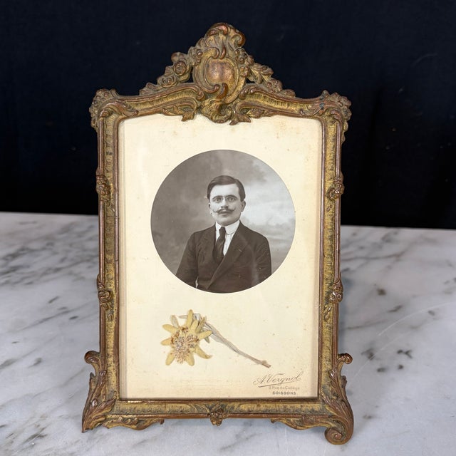 Charming antique French gilt metal tabletop photo frame with an ornate Rococo-inspired crest and finely cast scrolling...