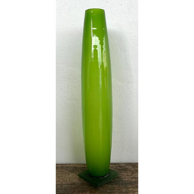 This vintage tall glass vase presents a dramatic, elongated cylindrical form in vivid, saturated apple-green glass, its...