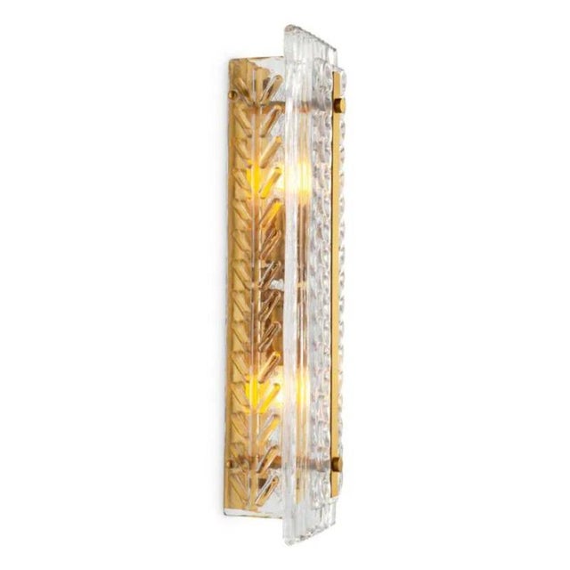 Pair of contemporary wall lamp in an antique brass finish and layered handmade glass, designed to provide soft,...