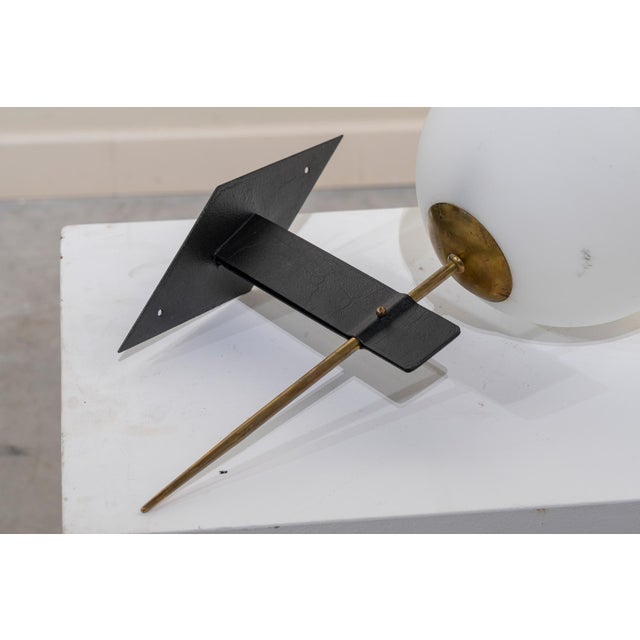 Pair of French wall sconces from the 1960s with white opaline glass globes and black metal and brass brackets. The wall-...