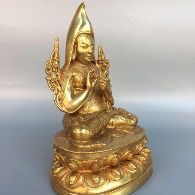 This finely crafted seated Tsongkhapa statue is cast from brass with a gilded finish, featuring intricate carving details...