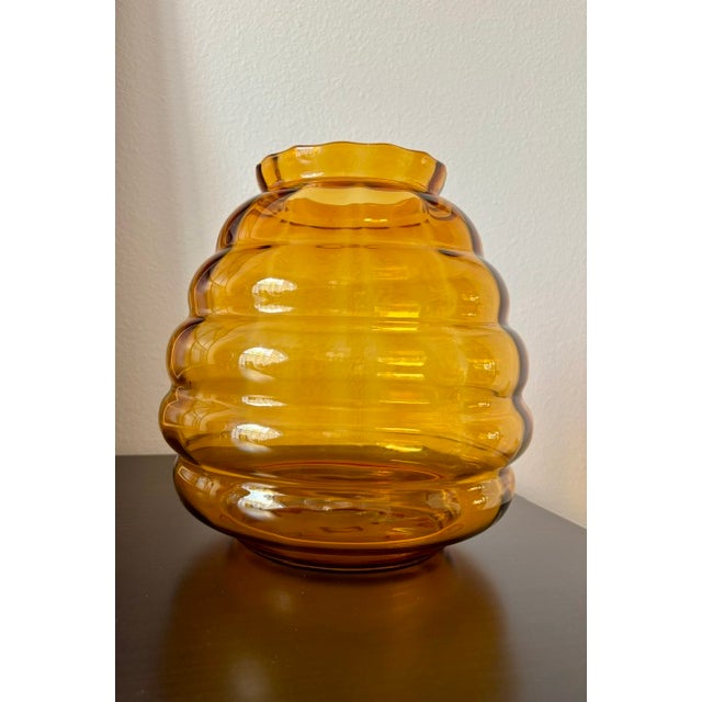 A striking amber glass vase featuring a rounded, beehive-inspired silhouette with pronounced horizontal ribs and a softly...