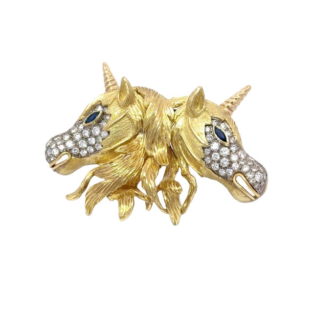 A captivating brooch showcasing two unicorns crafted in 18k yellow gold. Each unicorn is adorned with large bright white...