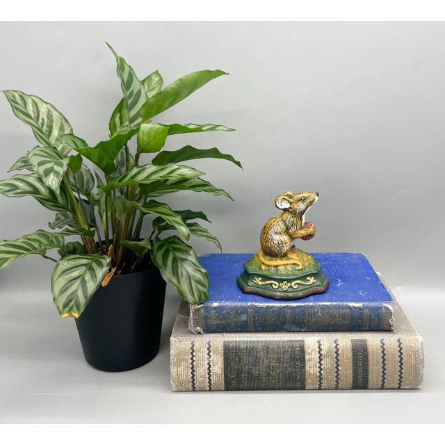Adorable cast iron doorstop featuring a wide-eyed mouse perched upright on a leafy green base, clutching a red berry in...