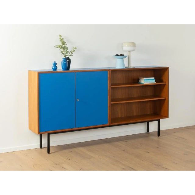 A wonderful sideboard from the 1960s. The body is made of teak veneer with two cabinet doors, four shelves, and new black...