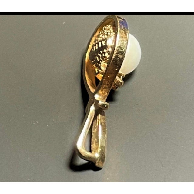 This elegant pendant features an openwork teardrop frame in polished 14k yellow gold, accented by a stylized crossed...