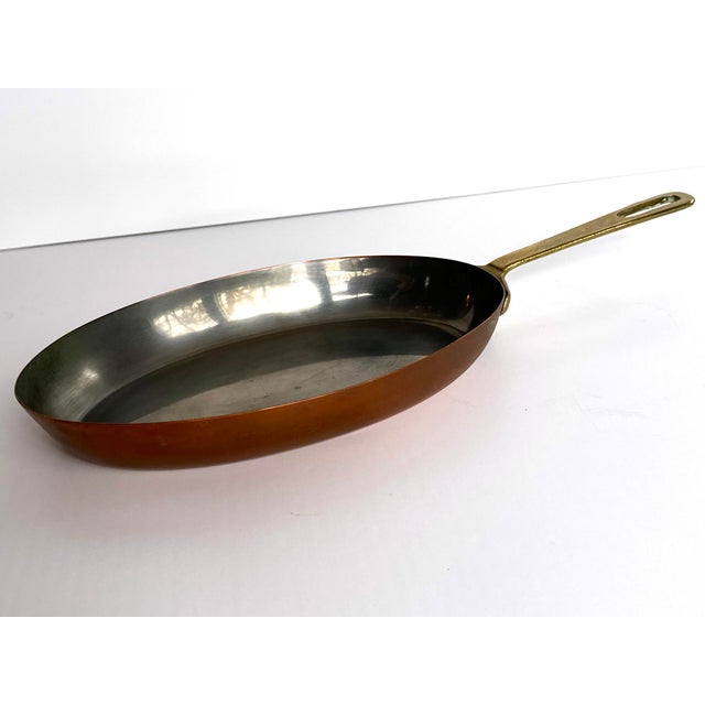 A fine antique French oval copper sauce pan featuring a sturdy brass handle secured with traditional copper rivets....