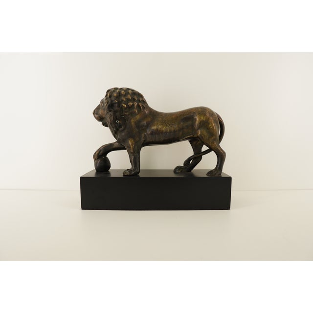 This vintage bronze lion sculpture captures a proud, confident stance with one paw resting atop a sphere, a classic symbol...