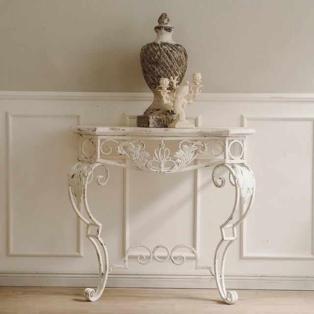 The console table is a newly produced piece of furniture featuring a bevelled wooden top and an openwork metal frame made...