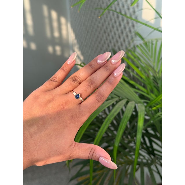 This cluster engagement ring features a 0.67 carat of pear-shaped blue sapphire set in 14K yellow gold. The sapphire...