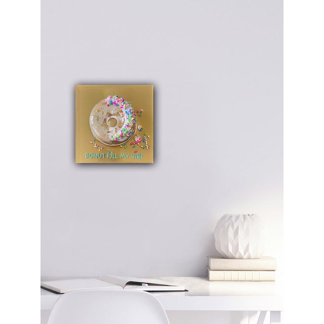 This mixed media piece features a glossy donut adorned with vibrant sprinkles, set against a shimmering gold background....