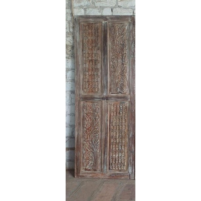 These vintage hand-carved wood sliding barn doors feature elegant floral motifs and a richly aged natural patina....