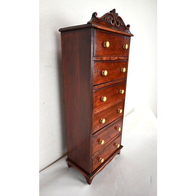 Small piece of furniture in mahogany opening by six identical drawers with ecru colored knobs. Its cornice is slightly...