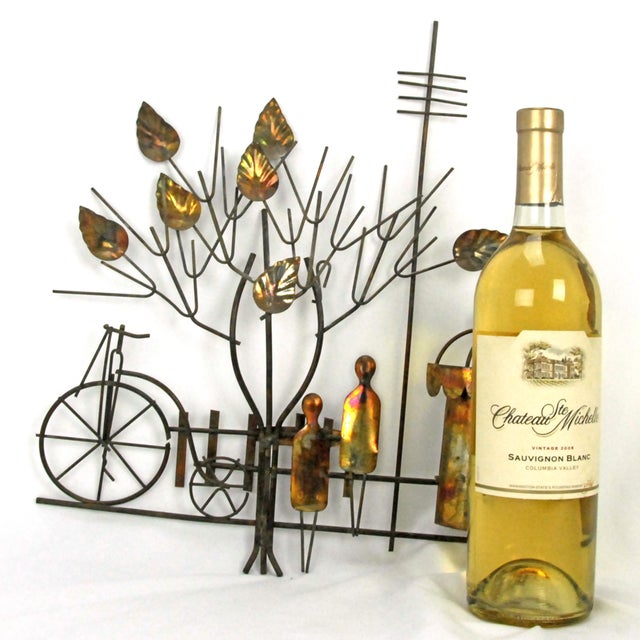 A vintage Enesco imports wall hanging from 1974 that features a whimsical metal scene with a tree, bicycle, and figures....