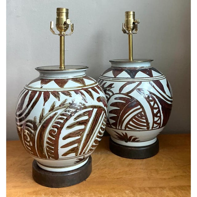 This pair of vintage ceramic lamps presents a full, globular silhouette with a short, flared neck and a softly rounded...