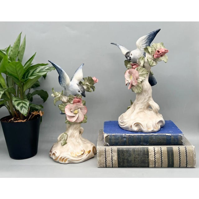 Lovely pair of vintage porcelain bird figurines, each featuring a blue and white bird in flight above soft pink flowers...