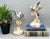 Lovely pair of vintage porcelain bird figurines, each featuring a blue and white bird in flight above soft pink flowers...