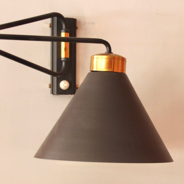 This articulated swing-arm wall light was designed by Rene Mathieu and was produced by Lunel in France. It has a cone lamp...