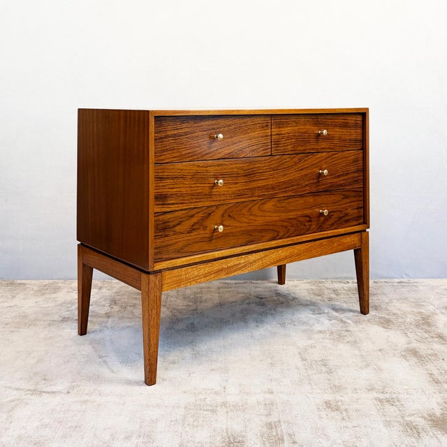 Constructed in walnut veneer over a plywood carcass, with dovetailed drawer boxes and a solid timber base and tapered...