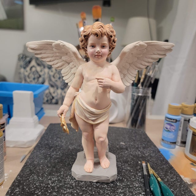 This standing cherub opens its feathered wings while one hand rests gently over the chest. An ivory drape, warm painted...