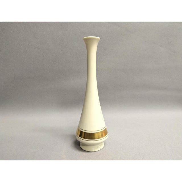 A tall cream and gold bud vase from Lenox china. The porcelain vase is from the Minaret collection and has three gold...