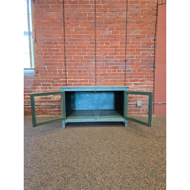 Bring a pop of soulful color and rustic utility to your space with this vintage industrial low cabinet. Featuring a...