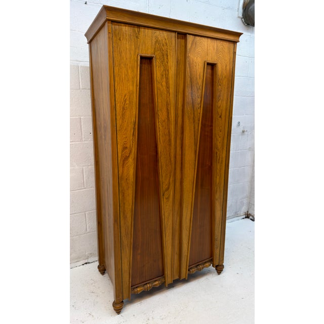 Distinctive vintage armoire crafted in warm golden-toned wood, featuring striking contrasting wood panels and beautifully...